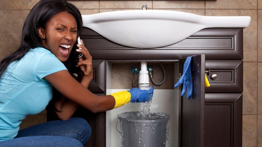 Concerned woman on the phone while trying to stop a leak under her sink