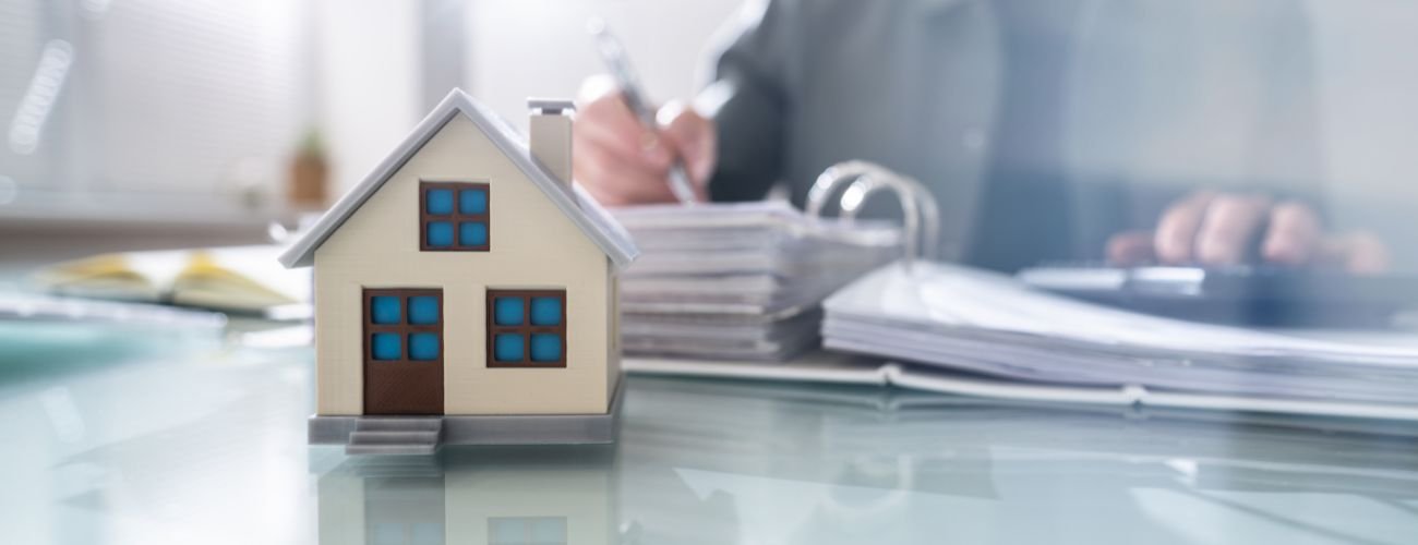 Real estate office with agent going through paperwork and small house sitting on table